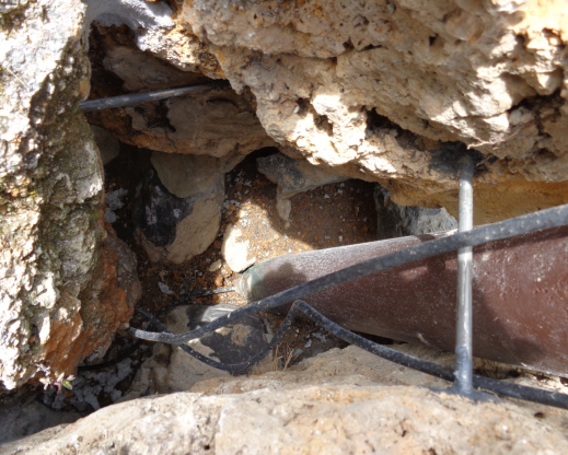 The space between the slabs forming the base of the tufa tower showing the two steel bars, the irrigation tube going into the base of the four-inch (10 cm) pipe, the two irrigation tubes beside the pipe, and the mortar between south and west slabs at the upper left. The space between the slabs forming the base of the tufa tower showing the two steel bars, the irrigation tube going into the base of the four-inch (10 cm) pipe, the two irrigation tubes beside the pipe, and the mortar between south and west slabs at the upper left.